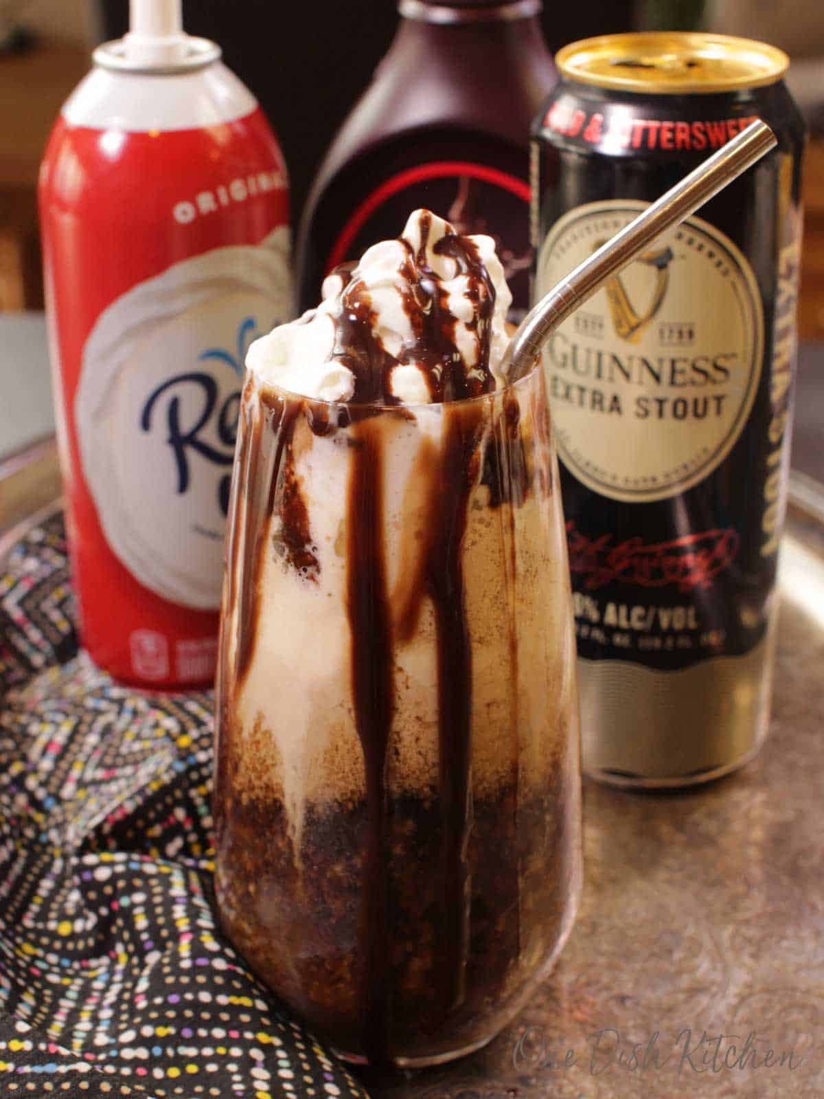 a Guinness Float on a silver tray made with ice cream and topped with whipped cream and chocolate syrup. The can of whipped cream and chocolate syrup is in the background. | one dish kitchen