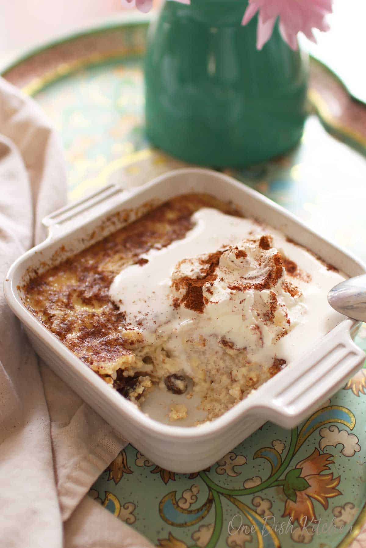 A spoonful missing from the homemade rice pudding topped with whipped cream and ground cinnamon in a small baking dish