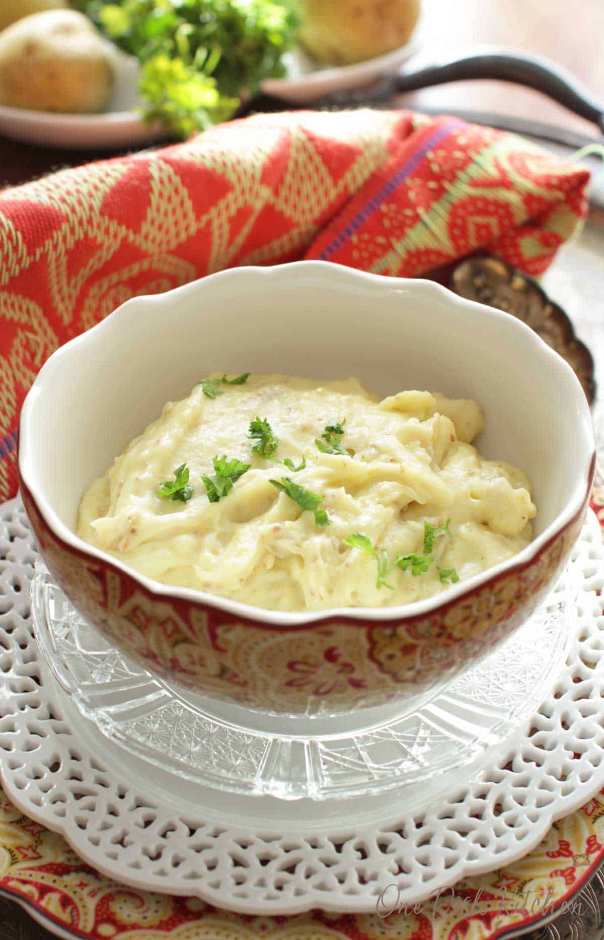 A bowl of mashed potatoes topped with parsley plated next to a red cloth napkin
