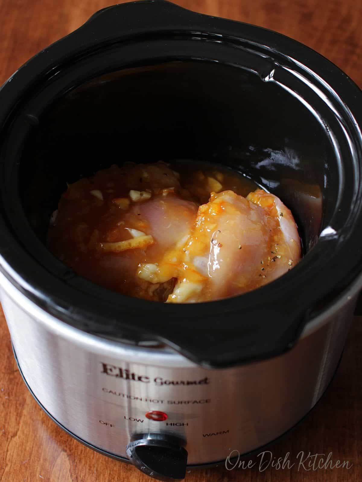 Raw chicken in an orange sauce in the base of a slow cooker