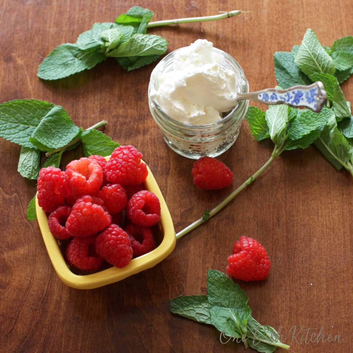 berries in a bowl and homemade whipped cream in a bowl with sprigs of fresh mint scattered on a table | one dish kitchen