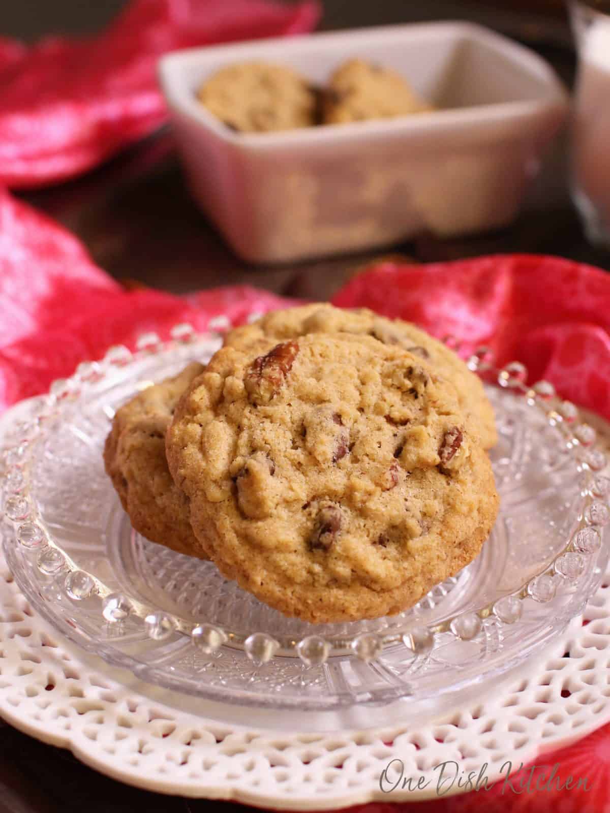 A small plate of three doubletree cookies surrounded by a red silk cloth with a dish of cookies in the background