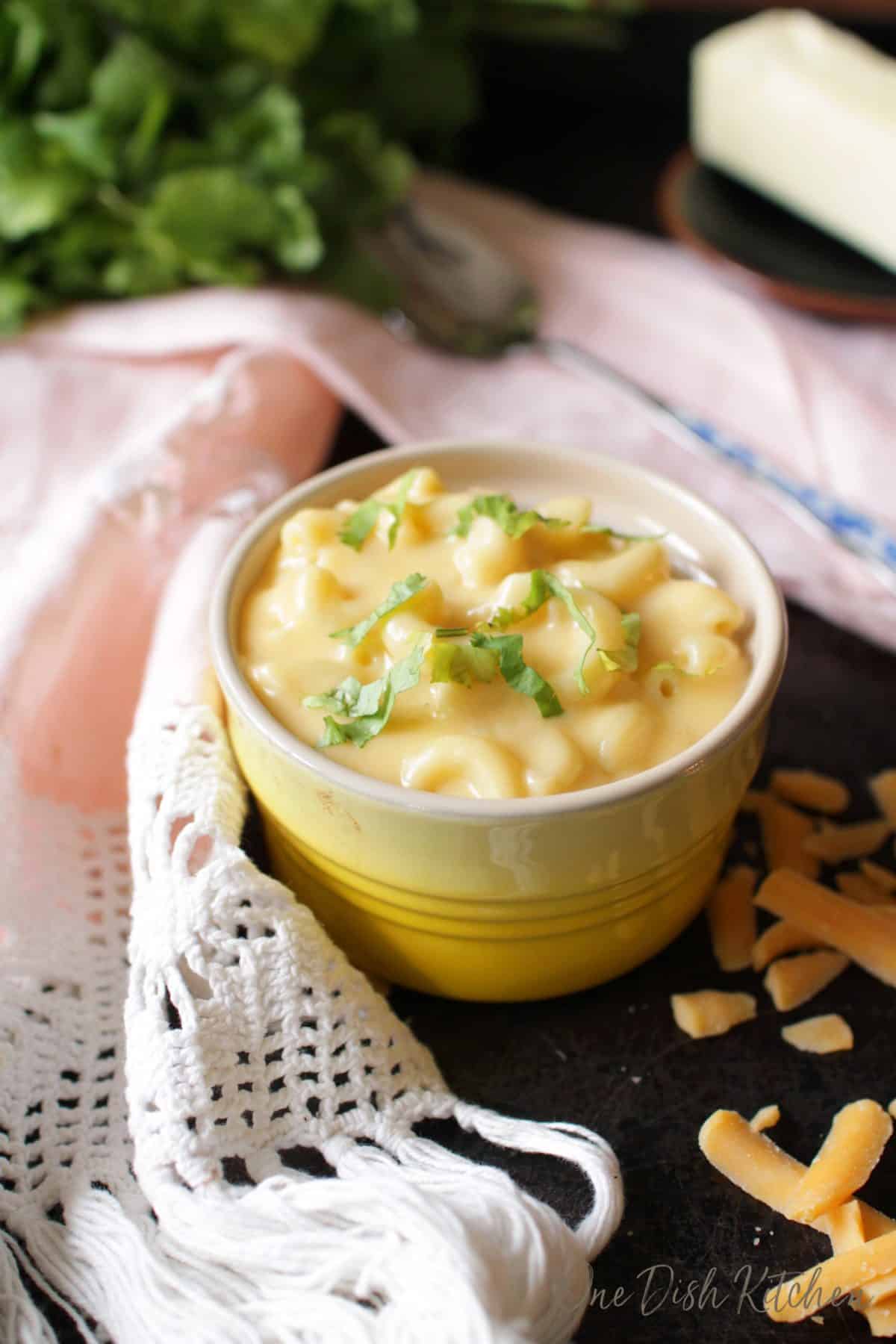 A small bowl of macaroni and cheese on a metal tray next to a spoon and a pink cloth napkin.