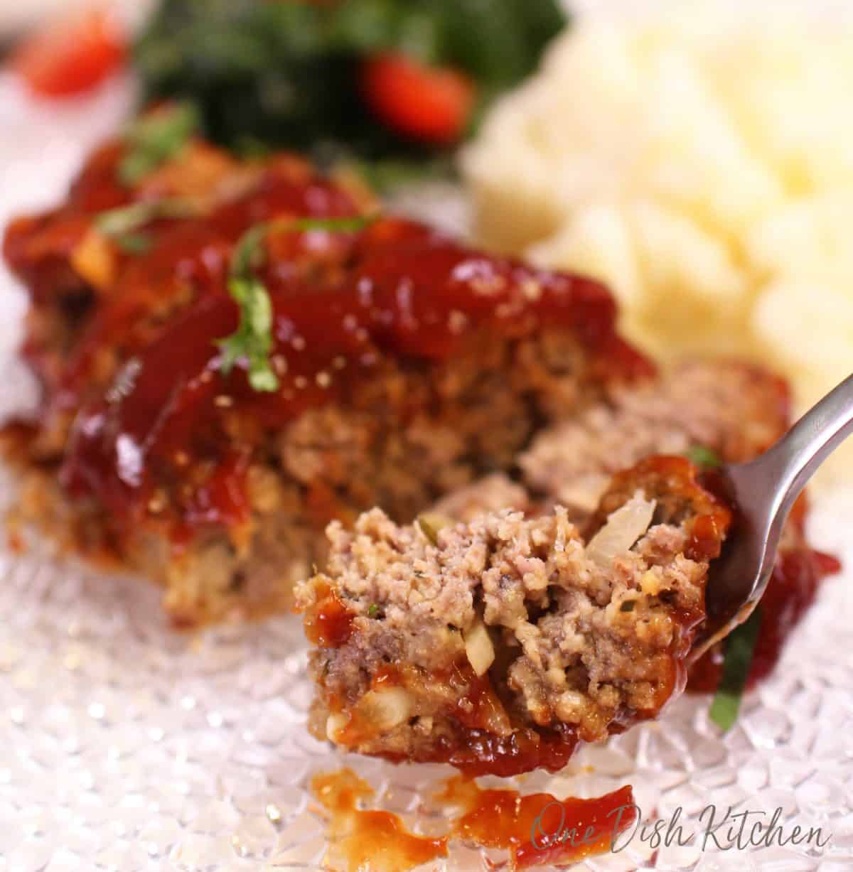 A forkful of meatloaf from a plate with mashed potatoes and a side salad