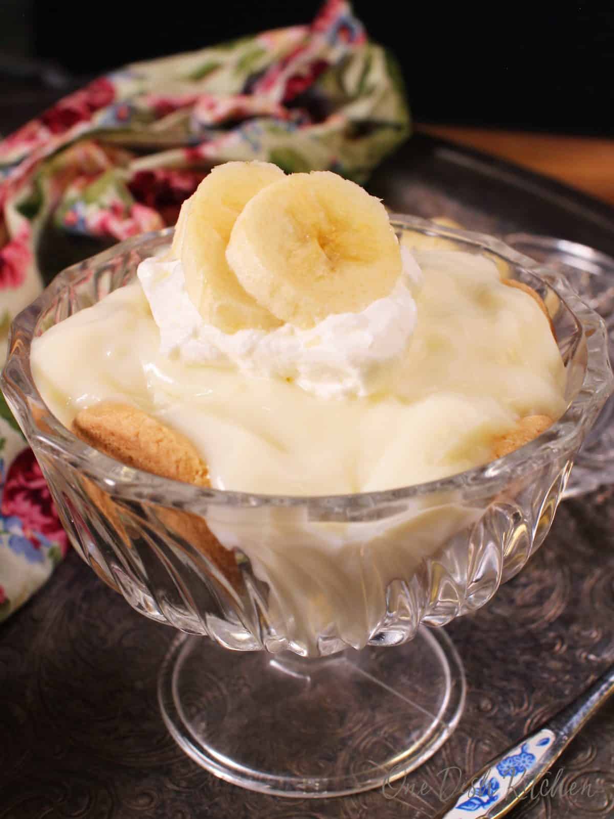 banana cream pie in a dessert dish topped with whipped cream and sliced bananas.