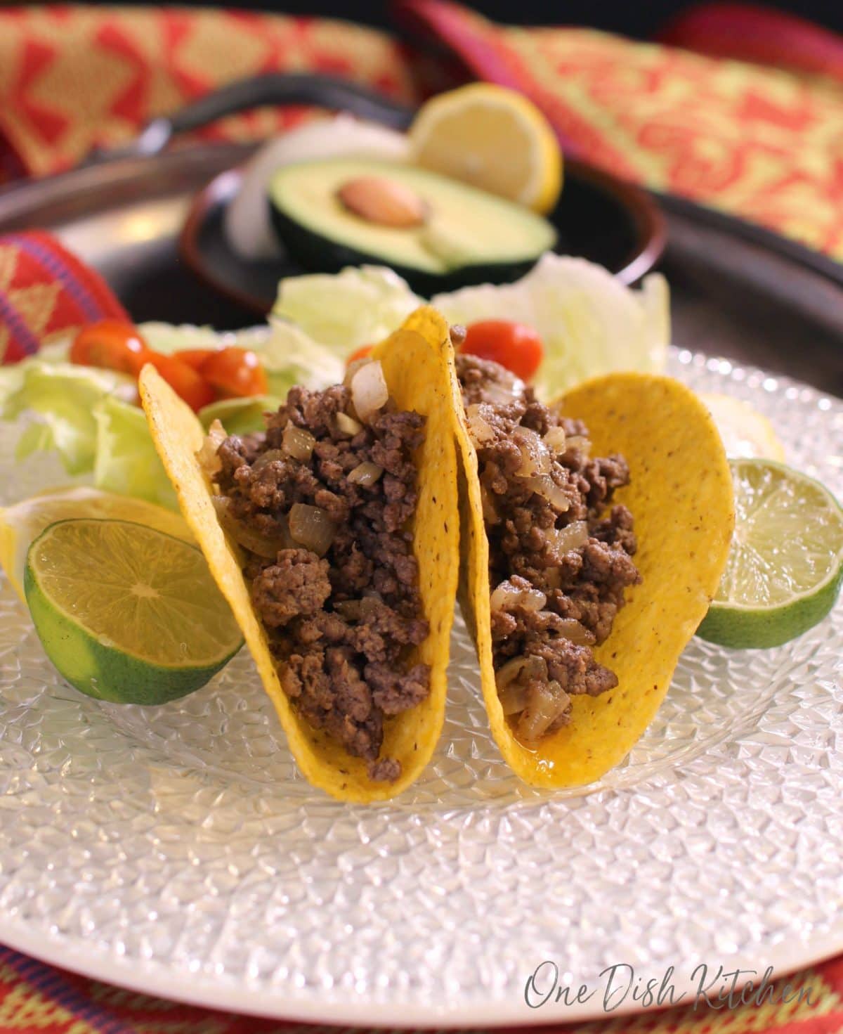 Two taco shells on a plate filled with ground beef and onions. The tacos are being held up by limes.