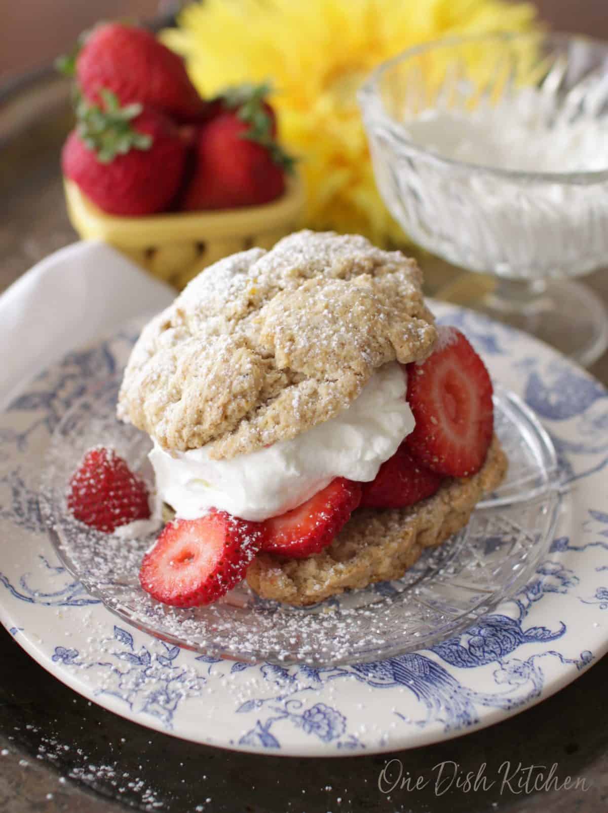 a strawberry shortcake on a plate with the top biscuit slightly falling off of the stack of strawberries.