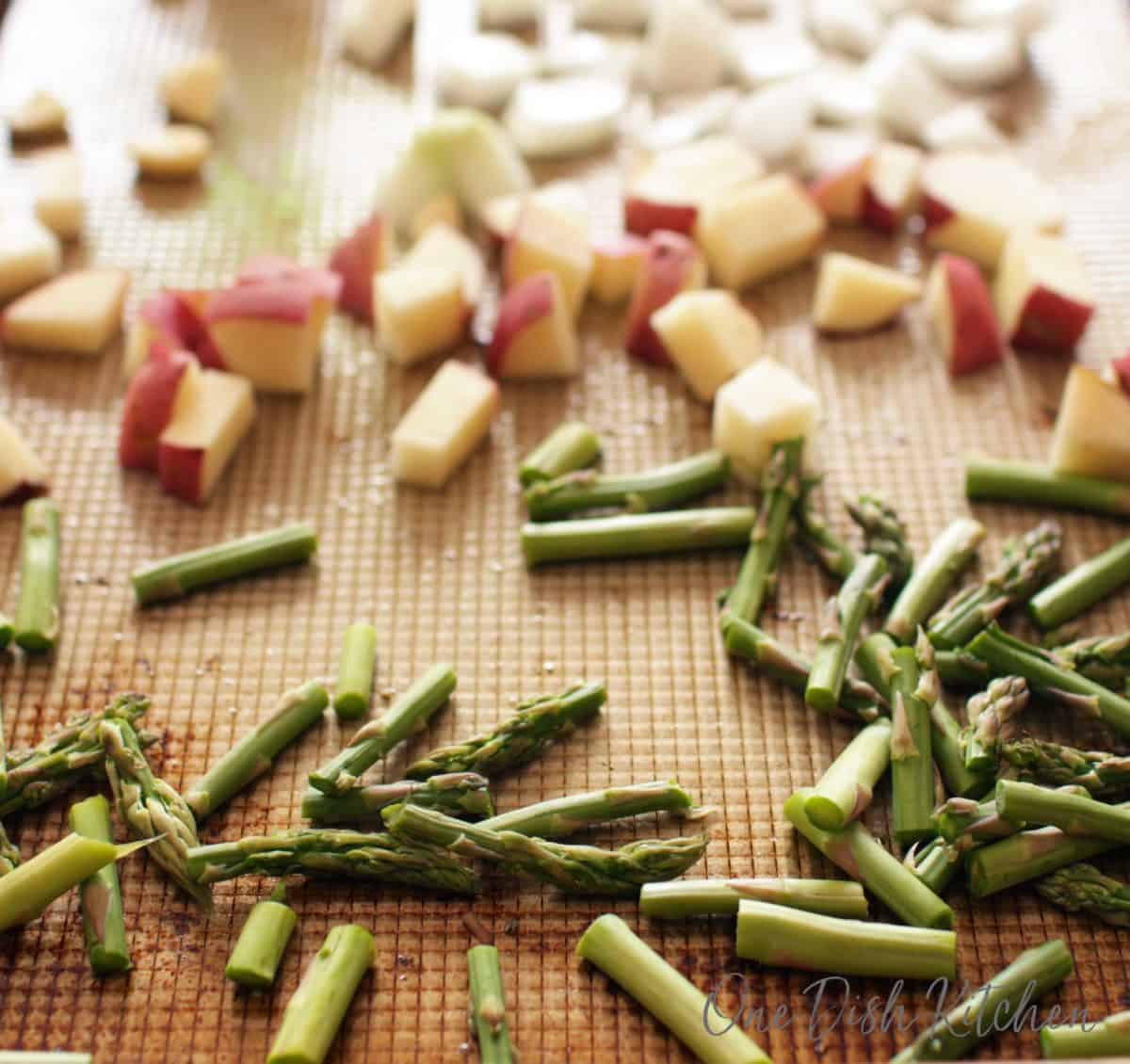 a baking tray filled with asparagus, potatoes, and onions.