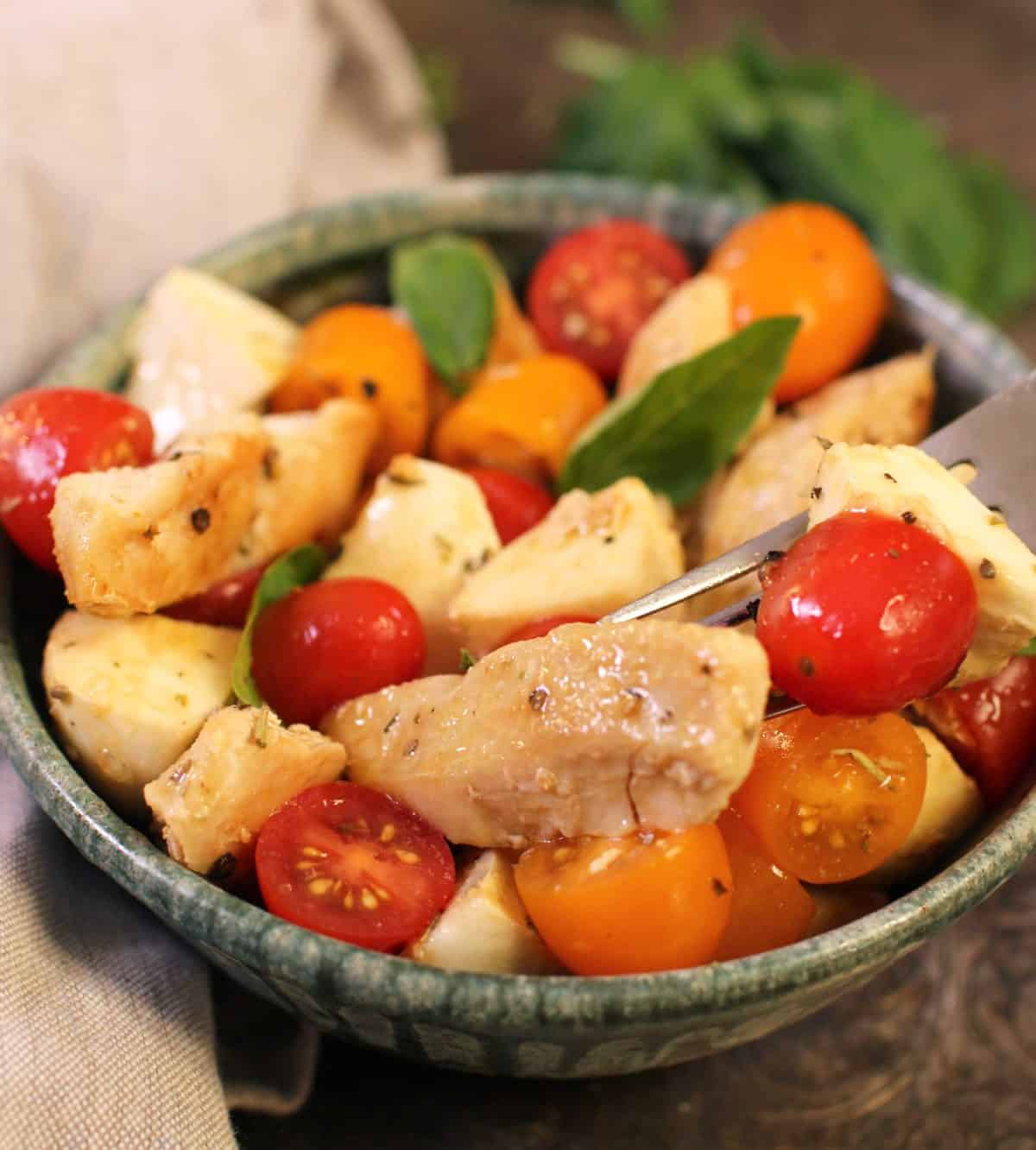 a fork filled with chicken and tomatoes on top of a bowl of salad.