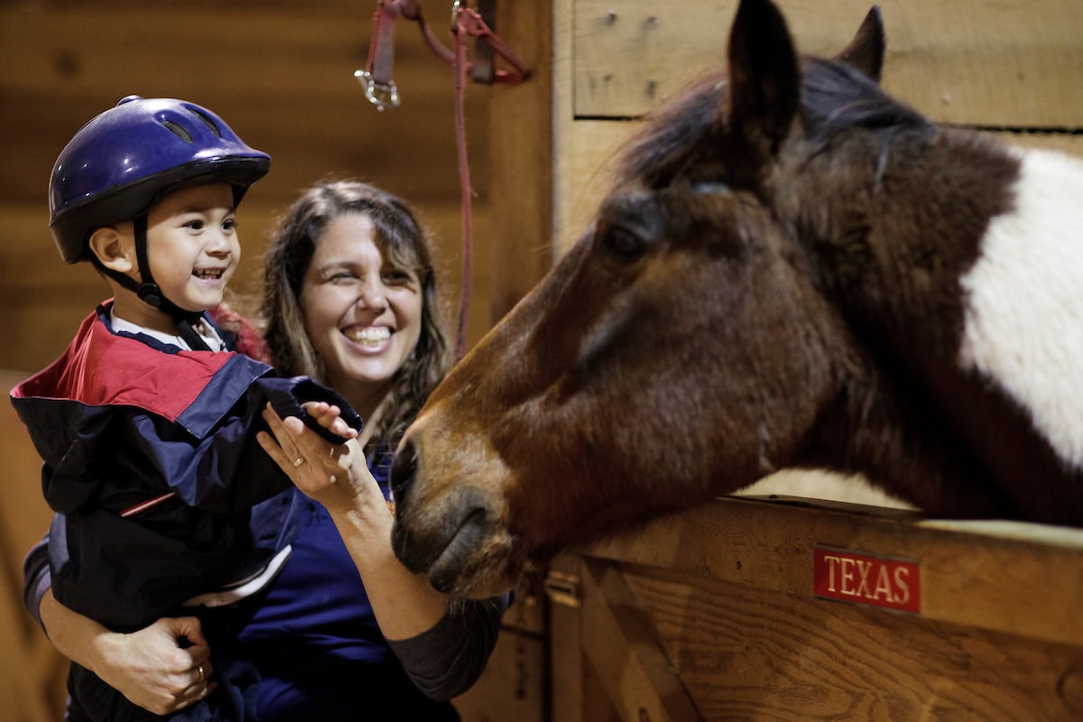 Nolina Varley, BU '01, an occupational therapist at Walker Therapy, helps a young boy greet a horse before an equine therapy session. (AJ Reynolds/Brenau University)