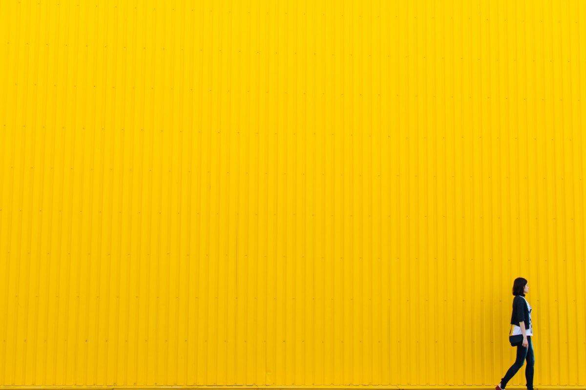 pedestrian walking in front of a bright yellow warehouse wall