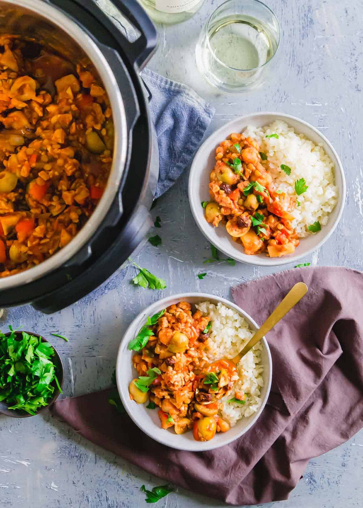 Picadillo with olives, lentils, tempeh and potatoes in one half of white bowl. White rice in other half of bowl.