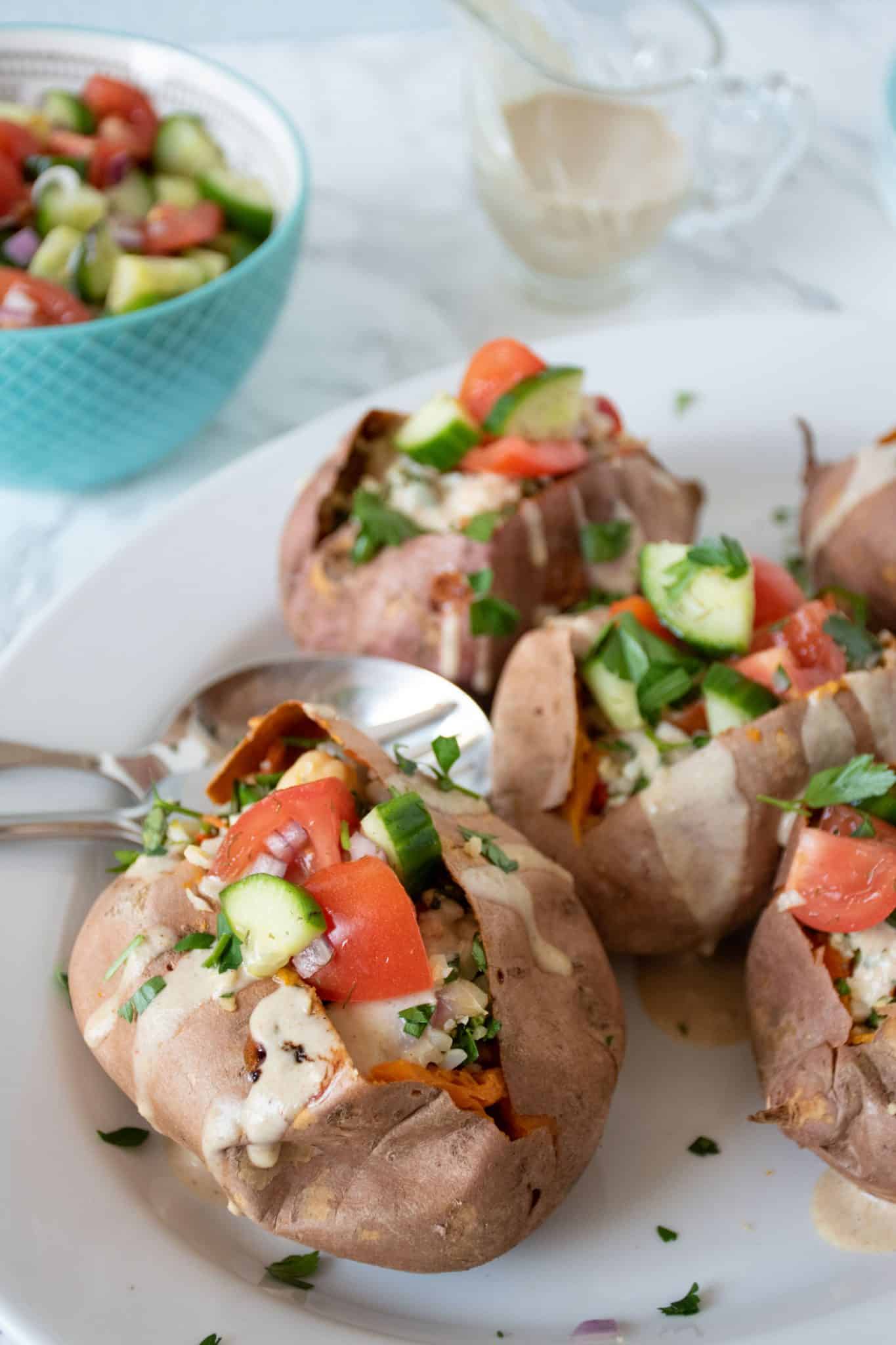 Stuffed sweet potatoes, topped with cucumber salad, and drizzled with tahini sauce, ready to serve.