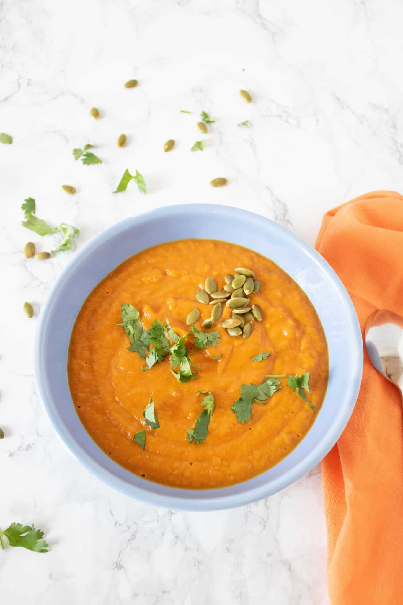 Overhead shot of pumpkin soup in a blue bowl, garnished with cilantro and pepitas.