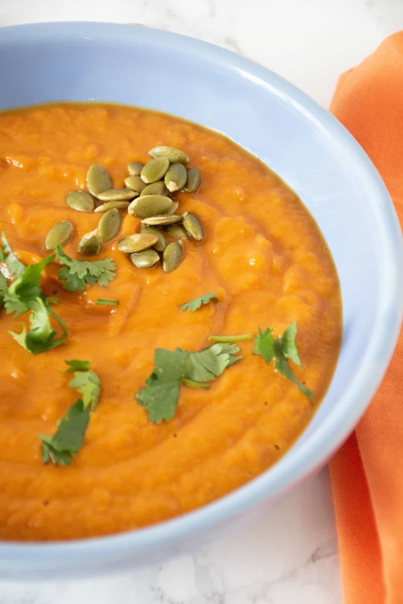 Pumpkin soup in a blue bowl, garnished with cilantro and pepitas.