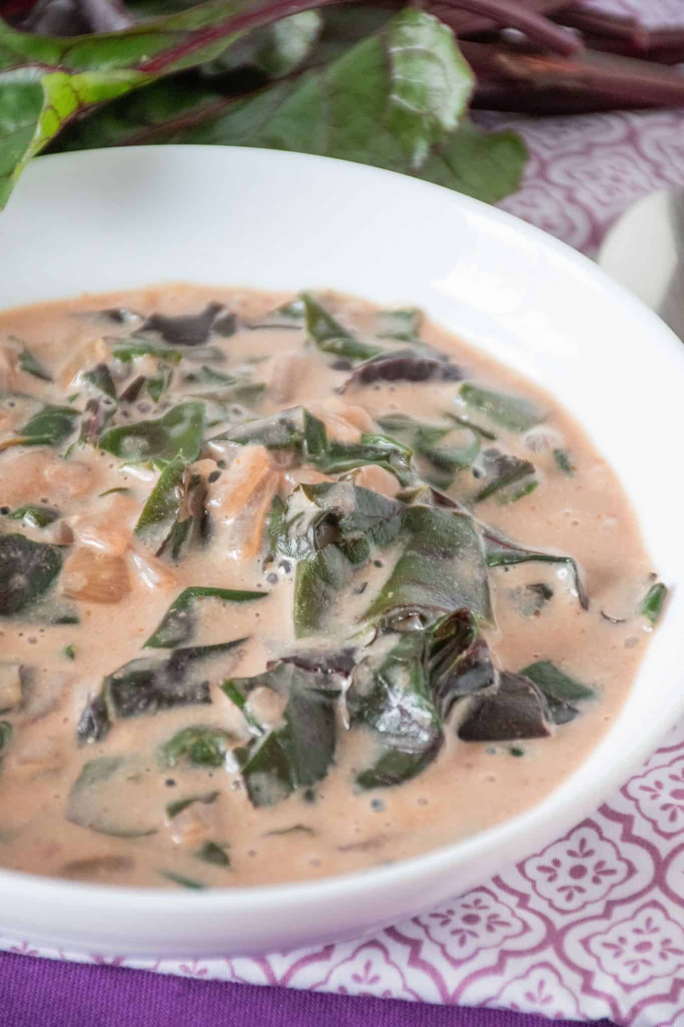 Close up of a bowl of braised greens in a light pink broth.