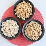 Three bowls of pasta on a red mat