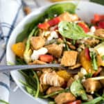 bowl of spinach salad with chicken, bell peppers, mandarin oraanges, and cheese with a white towel