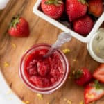 strawberry jam in a mason jar next to sliced strawberries on a cutting board