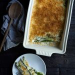 Asparagus gratin in a white casserole dish, next to one serving on a plate.