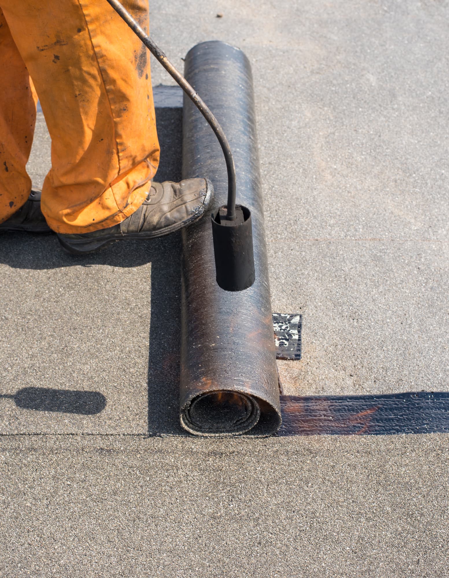Professional installation of waterproofing Roofer man worker at building site installing roll of roofing felt with gas blowpipe torch during construction works. flame during welding of a waterproofing membrane on a roof