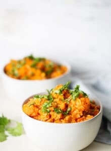 Two white bowls of vegan red lentil cauliflower curry topped with cilantro.