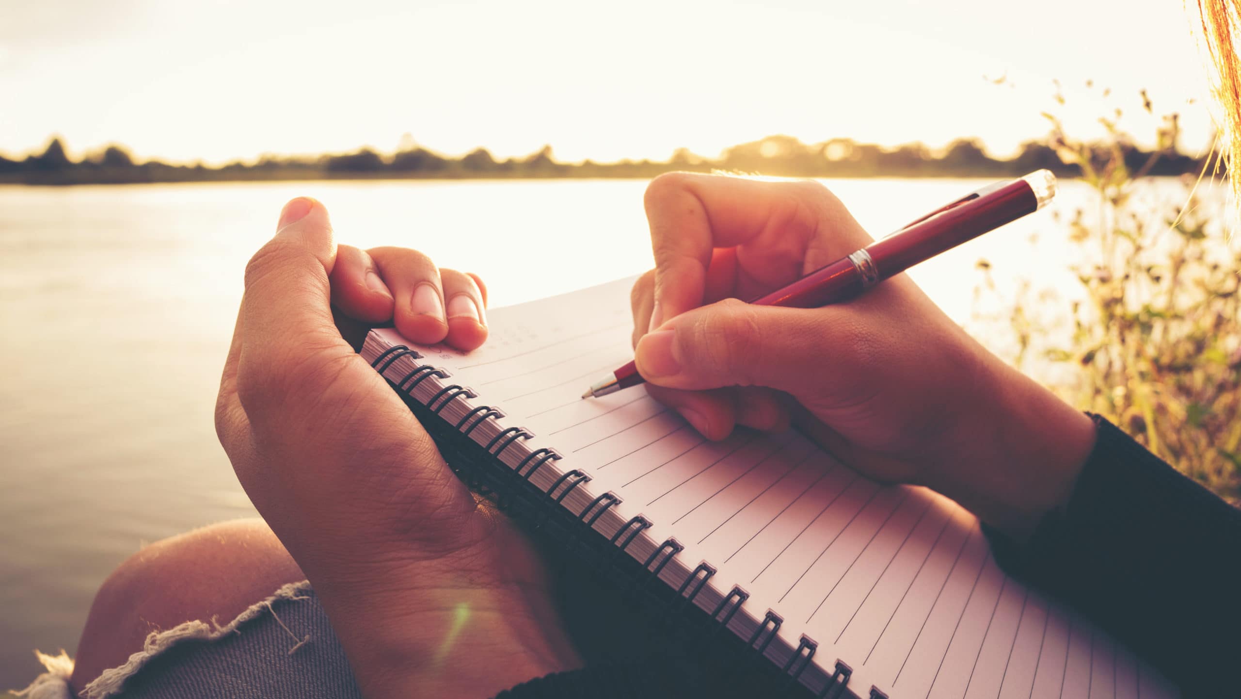 Person writing in journal near lake