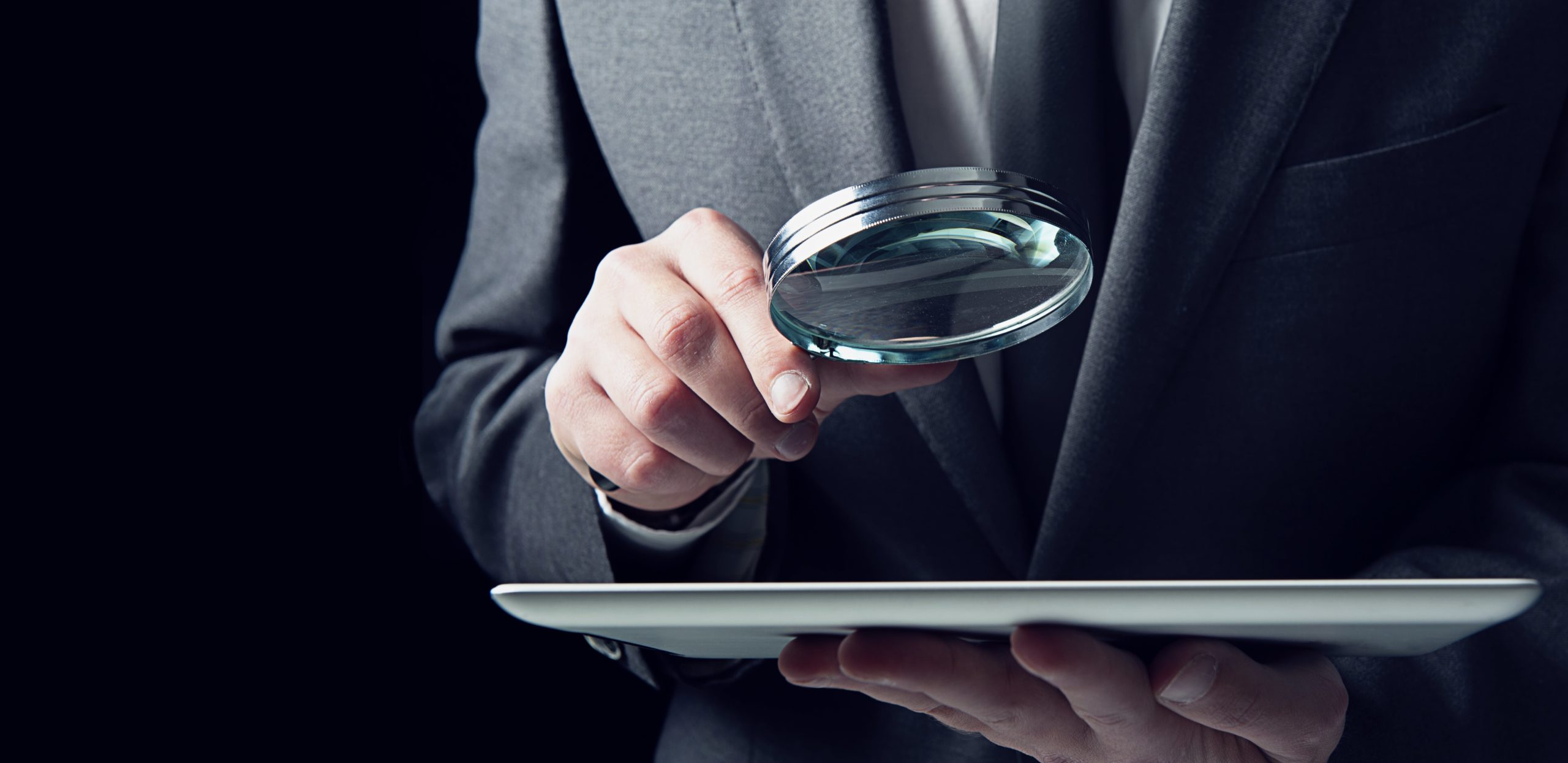 Other Investigations Man in suit holding magnifying glass looking at tablet
