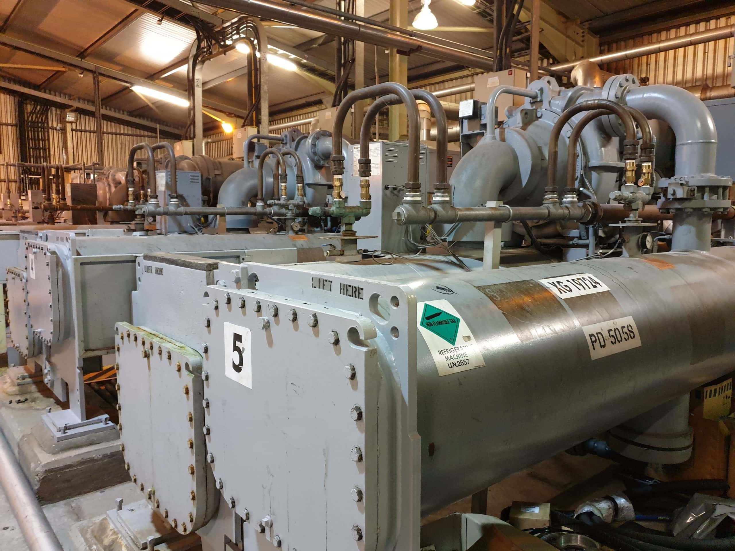 Plant room with row of 5 grey centrifugal chillers for service, maintenance and repair