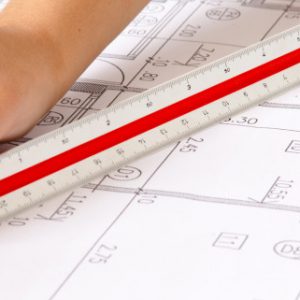Scale Ruler on Blueprints Two hands using a scale ruler on a set of blueprints