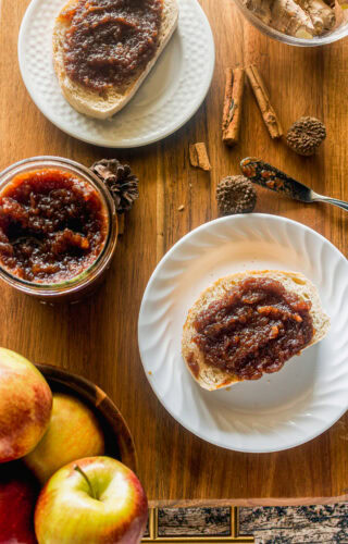 an overhead shot of a jar slow cooker apple butter with ingredients cinnamon, apples, and ginger on a platter with two plates of toast smeared with apple butter