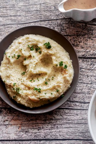 overhead of a plate of roasted garlic mashed potatoes and a gravy boat filled with turkey gravy
