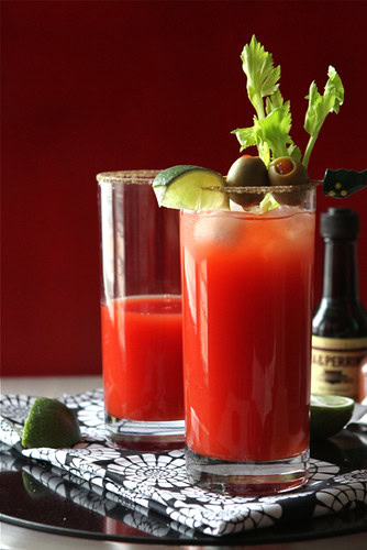 Red drink in tall glass garnished with green olives and celery