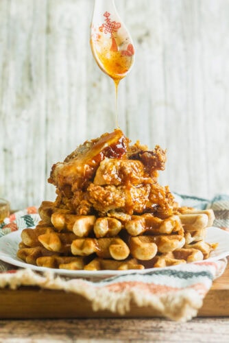a stack of waffles and southern fried chicken being drizzled with spicy honey butter