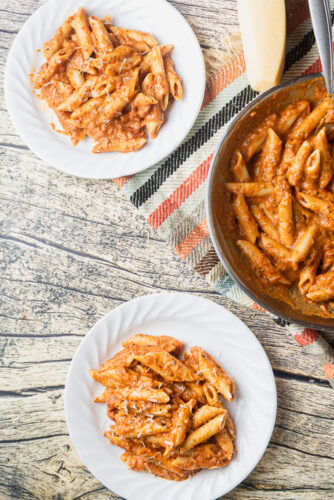 two plates and a pan of penne alla vodka are on a wooden table