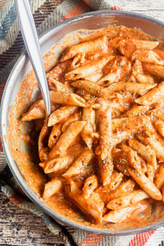 overhead shot of a full pan of vodka sauce with penne and a serving spoon in the pan