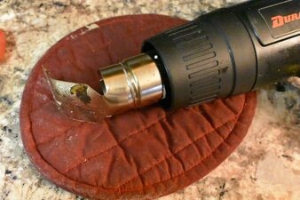Heat gun with flat metal attachment laying on hot pad.