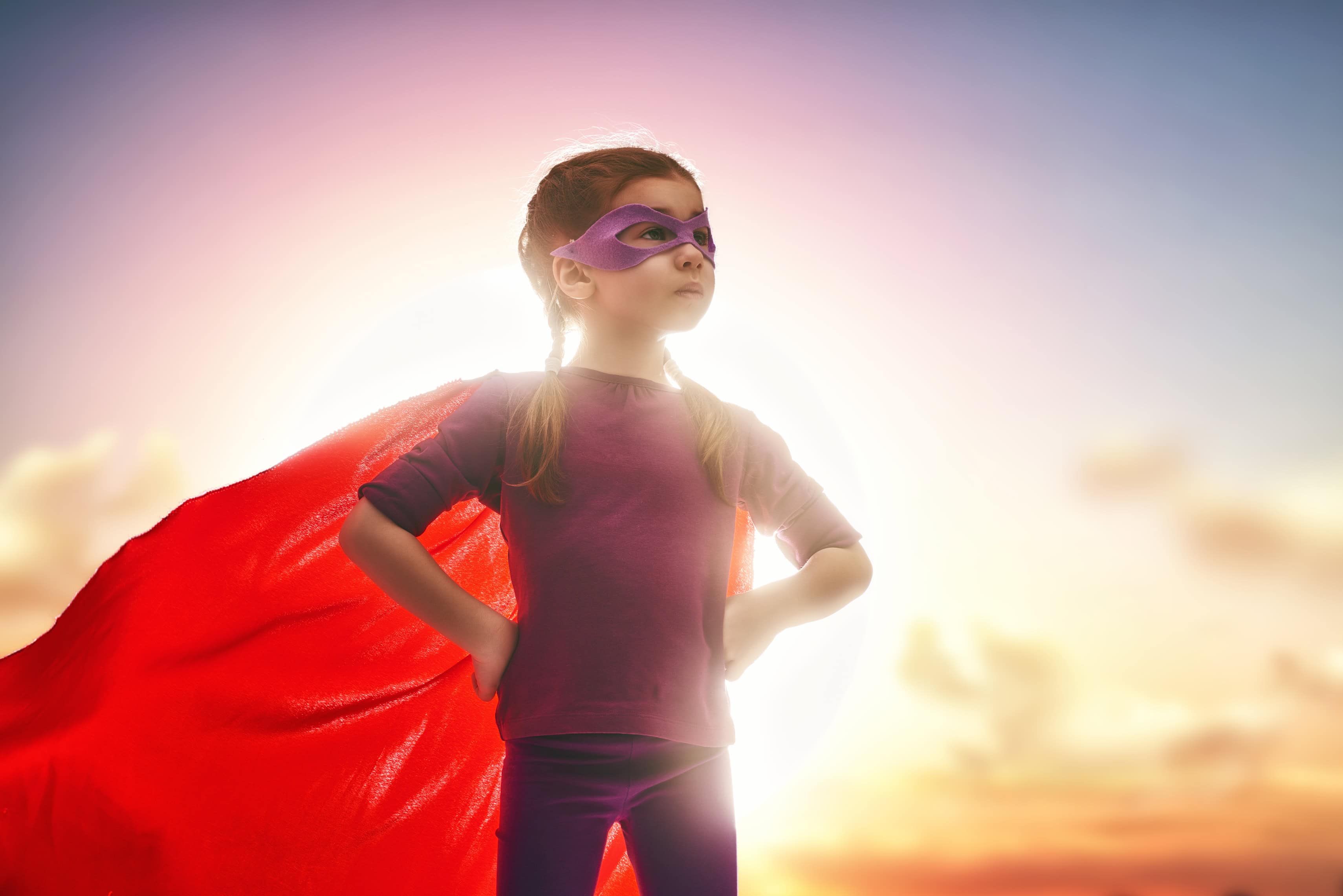 Little child girl plays superhero. Child on the background of sunset sky. Girl power concept
