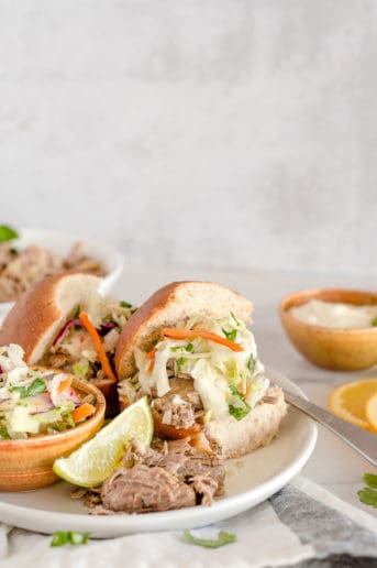 Pulled Pork Sandwiches on white plates topped with coleslaw and mayo