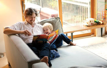 man reading book to happy child on couch