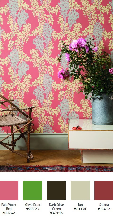 Cos'è lo stile d'arredo massimalista: interno con carta da parati floreale fucsia, sedia in vimini, tavolo basso laccato lucido bianco, vado di fiori in allumimio e tappeto rosso e blu