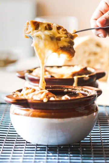 a spoonful of bread and cheese pulled from a bowl of traditional French onion soup