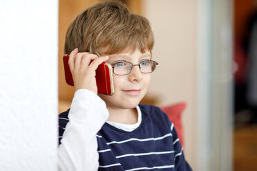 A photo of a young boy in glasses holding a red cell phone to his ear.