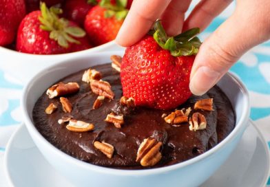 Strawberry being dipped into a bowl of brownie batter dip.