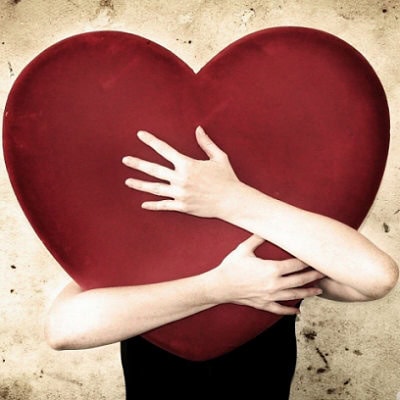 Mani che abbracciano un cuore rosso gigante