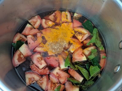 Tomatoes cooking in tamarind broth along with hing, curry leaves and turmeric powder