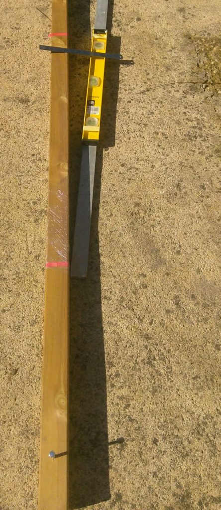 Sun shade post ready for concrete with hold-down bolts, protective plastic and tape for measuring angle of lean