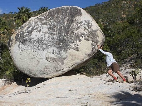 man pushing large boulder