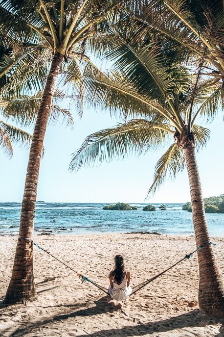 Siargao Itinerary And A girl sits on a hammock between two palm trees on Cloud Nine beach, SIargao