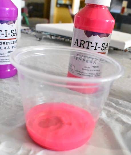 water poured into tempera paint in clear plastic cup